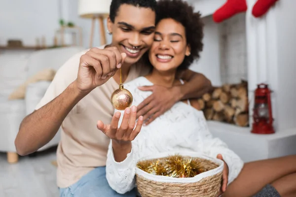 Feliz homem americano africano segurando bola de Natal de ouro perto alegre namorada — Fotografia de Stock