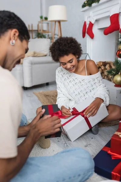 Heureux couple afro-américain ouverture cadeaux de Noël tout en étant assis sur le sol à la maison — Photo de stock