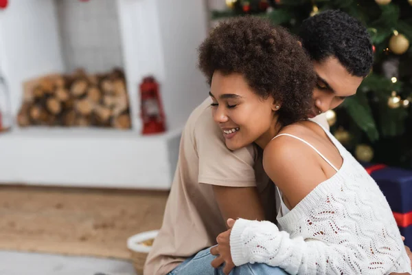 Sorridente mulher americana africana em suéter branco openwork abraçando namorado no dia de Natal em casa — Fotografia de Stock