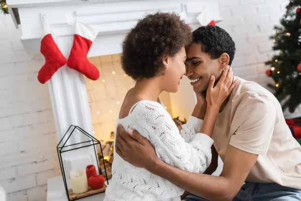 Jovem e feliz casal afro-americano abraçando perto de lareira com decoração de Natal — Fotografia de Stock