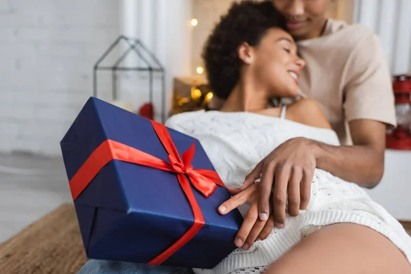 Selective focus of blue gift box with red ribbon near blurred african american couple — Stock Photo