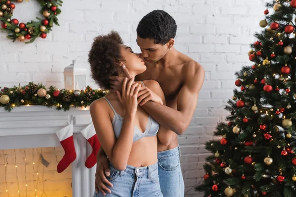 Junge und sexy afrikanisch-amerikanische Paar küsst sich in der Nähe von Weihnachtsbaum und dekorierten Kamin — Stockfoto