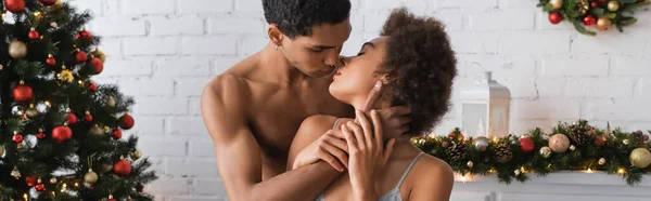 Appassionata coppia afroamericana con gli occhi chiusi baciare a casa vicino decorazioni natalizie, banner — Foto stock