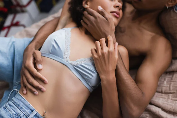 Сверху вид срезанной африканской женщины в лифчике рядом с мужчиной, обнимающим ее в спальне — стоковое фото