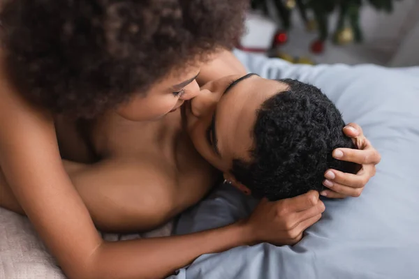 Curly african american woman hugging shirtless boyfriend lying on bed — Stock Photo