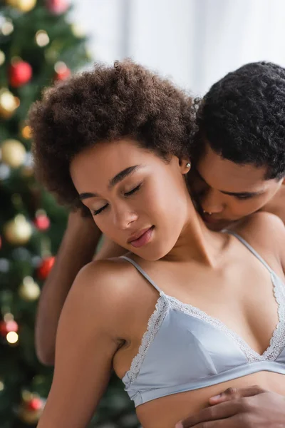 Young and sexy african american woman with closed eyes near boyfriend kissing her on blurred background — Stock Photo