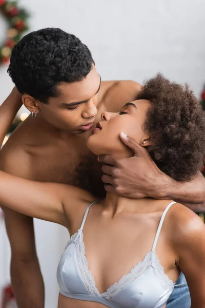 Hombre afroamericano con piercing abrazando el cuello de novia apasionada en sujetador de seda - foto de stock