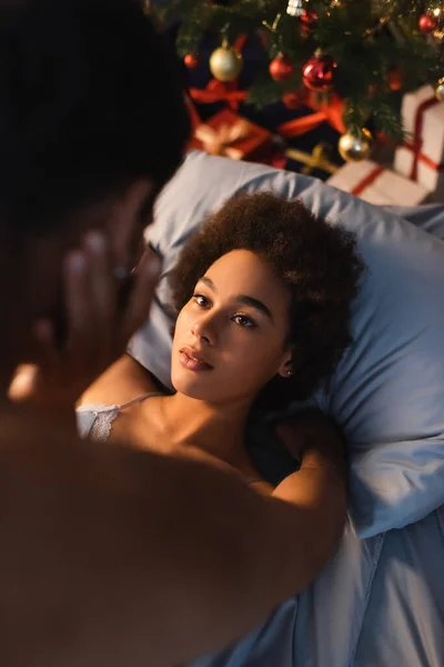 Vista ad alto angolo della donna riccia africana americana sdraiata sul letto e toccante fidanzato offuscato — Foto stock