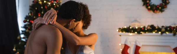 Сексуальна афроамериканська пара обіймає і цілує біля розмитих різдвяних прикрас, банер — стокове фото