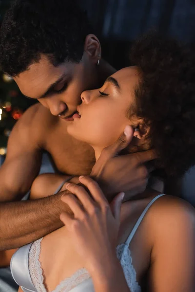 Sexy africano americano hombre abrazando cuello y besar apasionada mujer en sujetador por la noche - foto de stock