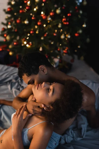 Homme afro-américain étreignant le cou et embrassant femme séduisante avec les yeux fermés — Photo de stock