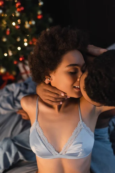 Соблазнительная и улыбающаяся африканская американка рядом с парнем целует ее в канун Рождества — стоковое фото