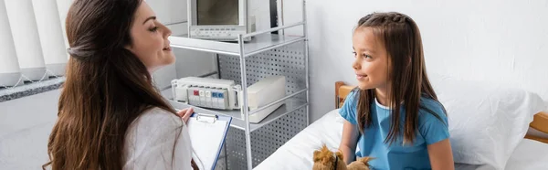 Médico sonriente con portapapeles mirando al paciente en la sala del hospital, pancarta - foto de stock