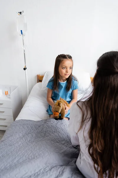 Kid holding soft toy and looking at blurred pediatrician in hospital ward — Stock Photo