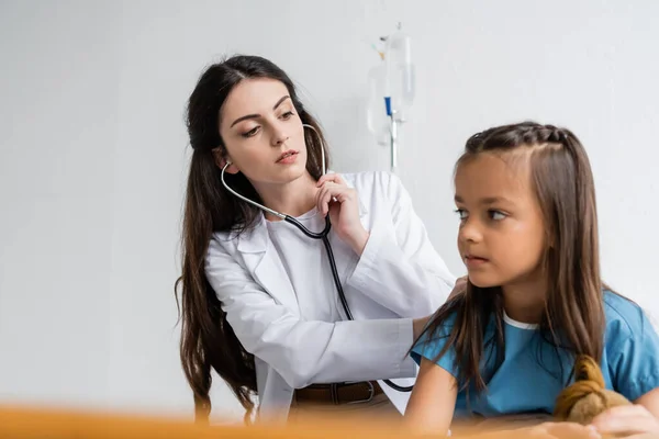 Pediatrician with stethoscope checking back of patient in hospital ward — Stock Photo