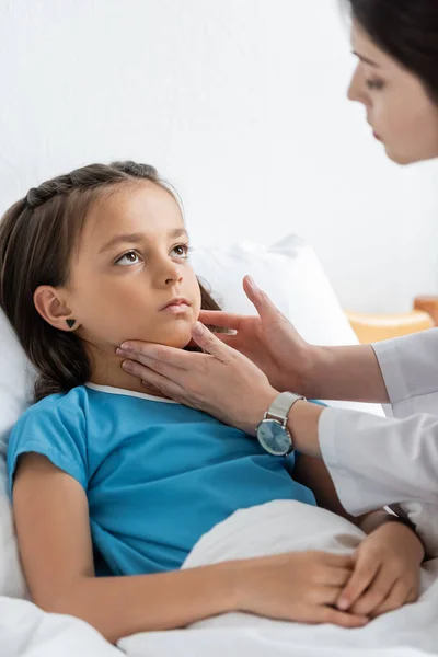 Médico borroso examinando el cuello del niño en la cama del hospital - foto de stock