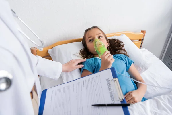 Médecin tenant masque à oxygène et presse-papiers près du patient sur le lit d'hôpital — Photo de stock