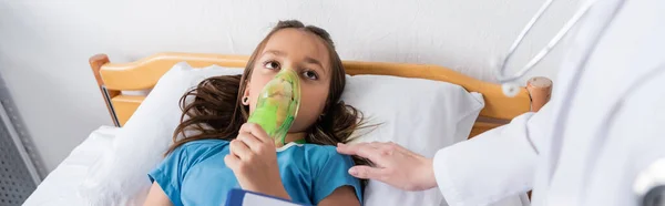 Niño sosteniendo la máscara de oxígeno y mirando al pediatra en la sala del hospital, pancarta - foto de stock