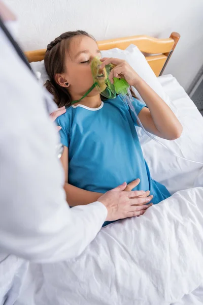 Médico tocando la mano del niño con máscara de oxígeno en la cama del hospital - foto de stock