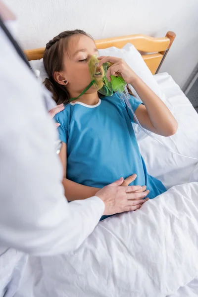 Doctor touching hand of child with oxygen mask on hospital bed — Stock Photo