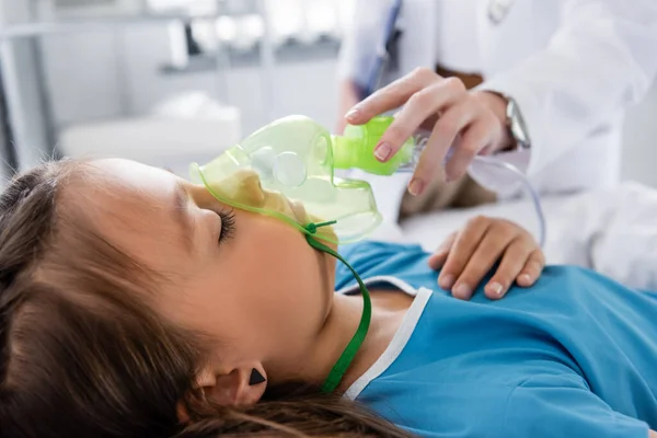 Размытый педиатр держит кислородную маску рядом с больным ребенком в больнице — стоковое фото