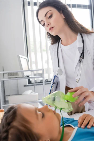 Pediatra con maschera di ossigeno e guardando il paziente in clinica — Foto stock