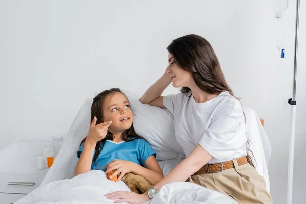 Criança com brinquedo macio conversando com a mãe na cama no hospital — Fotografia de Stock