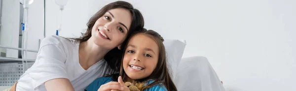 Mère et enfant souriant à la caméra sur le lit dans la salle d'hôpital, bannière — Photo de stock