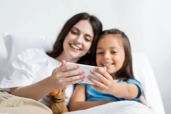 Позитивна жінка і дитина, використовуючи смартфон на ліжку в лікарні — стокове фото