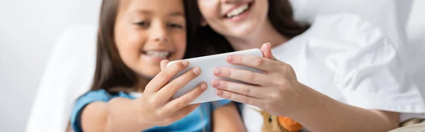 Размытые родитель и ребенок с помощью смартфона на кровати в клинике, баннер — стоковое фото