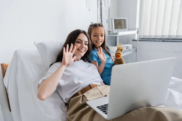 Donna sorridente e ragazza in abito paziente con videochiamata sul computer portatile nel reparto ospedaliero — Foto stock