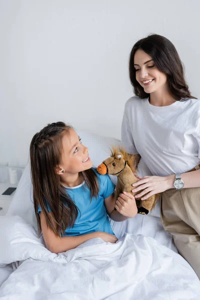 Un parent souriant tenant un jouet près d'un enfant au lit à la clinique — Photo de stock