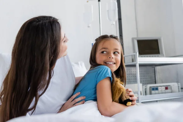 Mutter umarmt glückliche Tochter mit Spielzeug auf Krankenhausstation — Stockfoto
