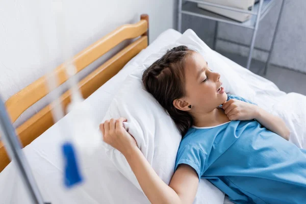 Vista de ángulo alto del niño enfermo acostado en la cama en el hospital - foto de stock