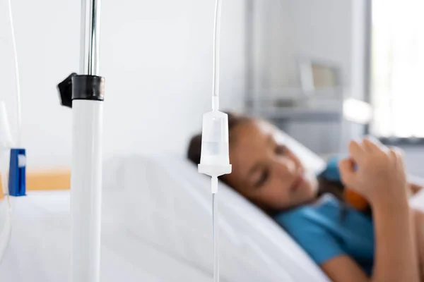 Traitement intraveineux sur pied près d'un enfant malade flou à l'hôpital — Photo de stock