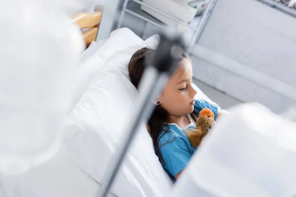 Visão de ângulo alto de criança doente com brinquedo deitado na cama n clínica — Fotografia de Stock