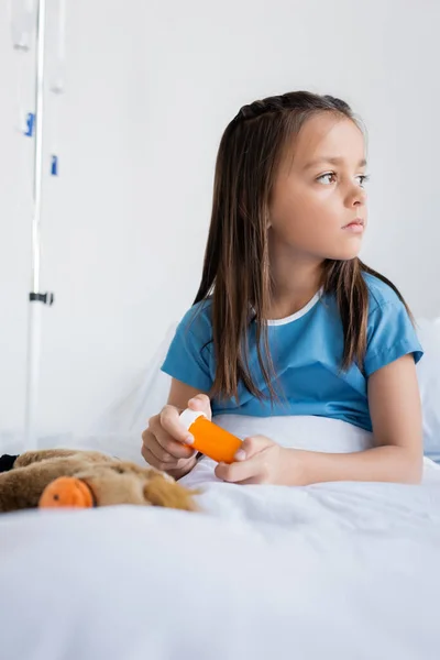 Ребенок в больничном халате держит таблетки на кровати в больнице — стоковое фото
