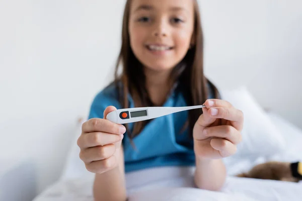 Blurred child holding electronic thermometer on bed in clinic — Stock Photo