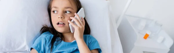 Enfant en blouse de patient parlant sur téléphone portable à l'hôpital, bannière — Photo de stock