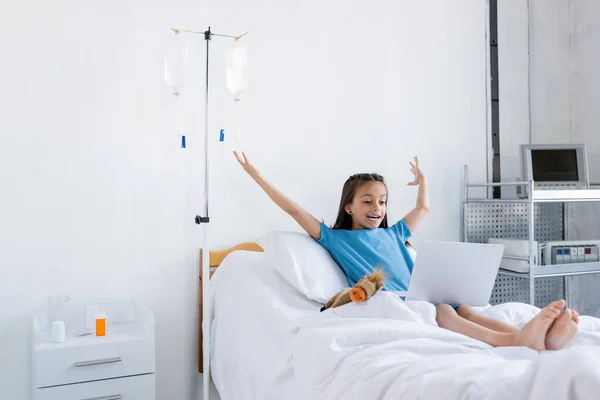 Excited kid using laptop near toy on bed in clinic — Stock Photo