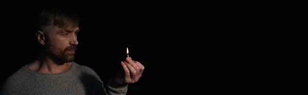 Homem segurando fósforo iluminado durante queda de energia isolado em preto, banner — Fotografia de Stock