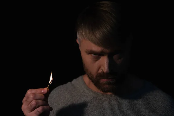 Angry man holding lit match and looking at camera during power blackout isolated on black — Stock Photo