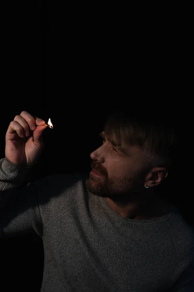 Чоловік дивиться на полум'я палаючого сірника під час відключення електроенергії ізольовано на чорному — стокове фото