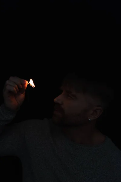 Uomo guardando fiamma di fiammifero ardente durante interruzione di corrente isolato su nero — Foto stock