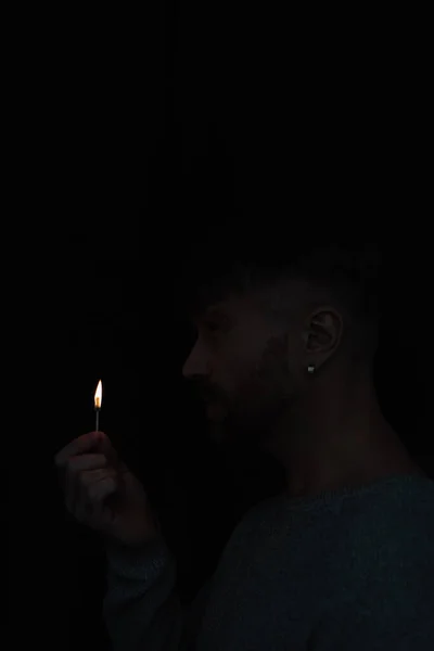 Seitenansicht eines Mannes mit brennendem Streichholz während eines Stromausfalls isoliert auf schwarz — Stockfoto