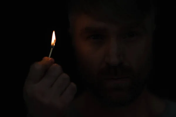 Close up view of man holding lit match and looking at camera isolated on black — Stock Photo