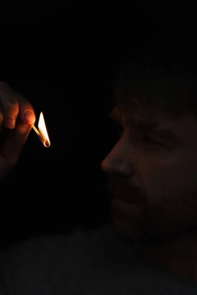 Homme regardant flamme de allumette brûlante dans l'obscurité isolé sur noir — Photo de stock