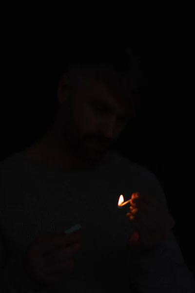 Hombre con caja de cerillas mirando partido ardiente en la oscuridad aislado en negro - foto de stock