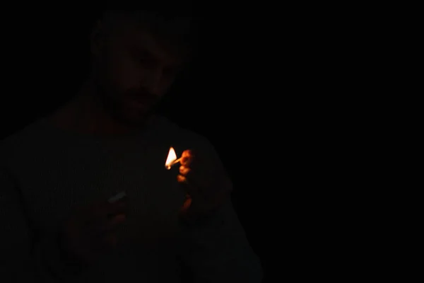 Hombre con caja de cerillas mirando partido ardiente durante apagón de energía aislado en negro - foto de stock