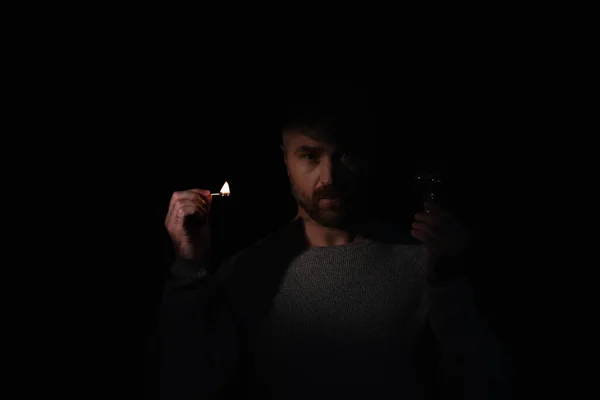 Человек с электрической лампочкой и зажженный спичкой глядя на камеру, изолированную на черном — стоковое фото